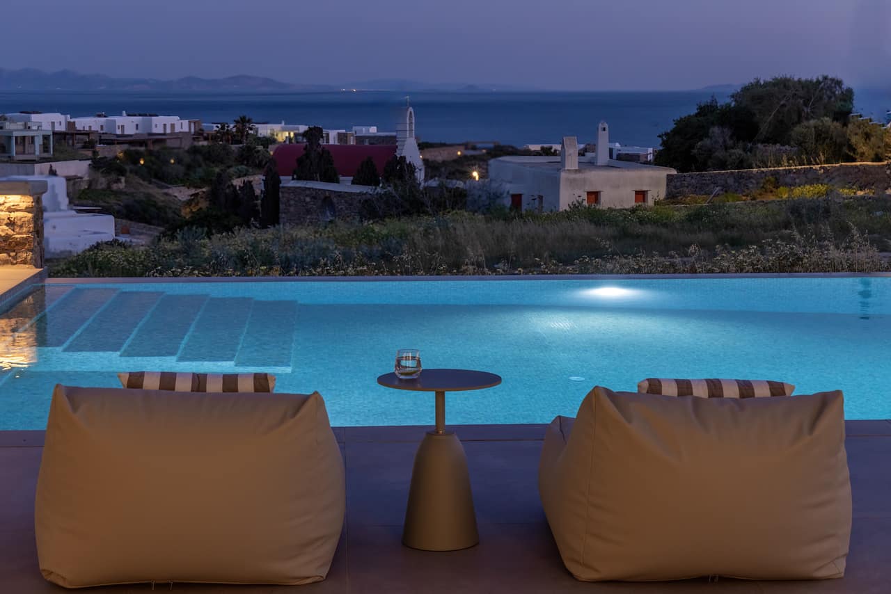 The pool at dusk, loungers facing the sea and a distant chapel